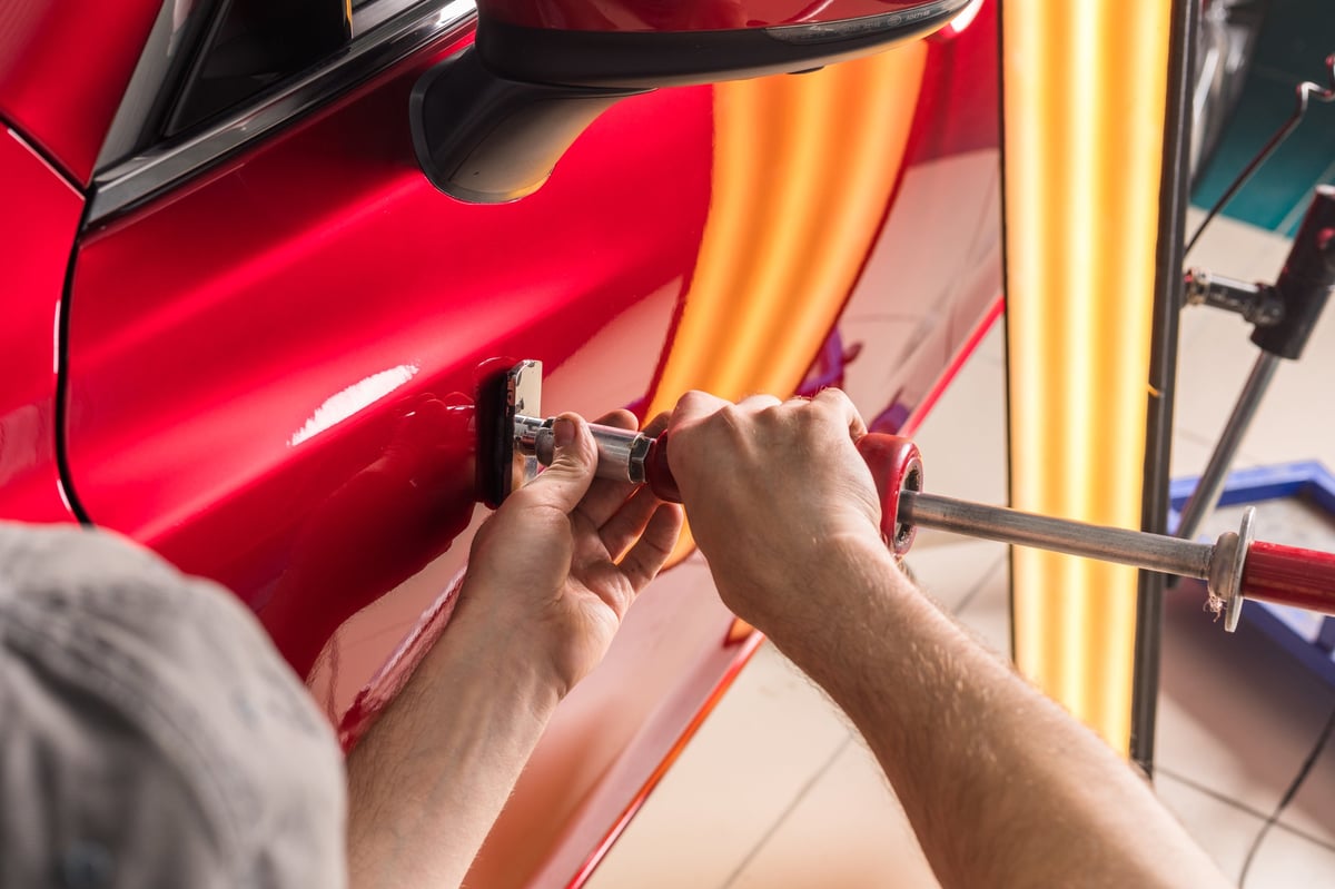 Technician removes dents on the car using the paintless dent repair method without painting