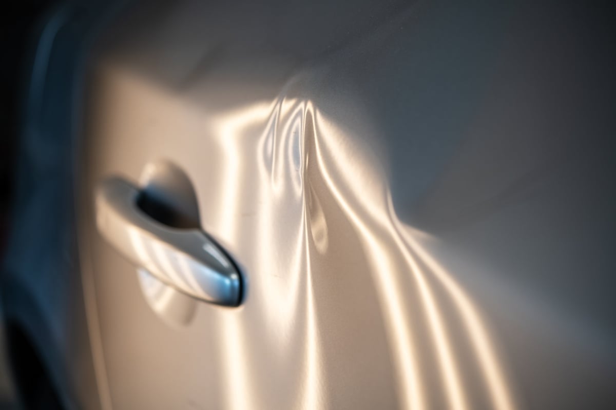 Close-up of a car door featuring multiple dents requiring professional repair
