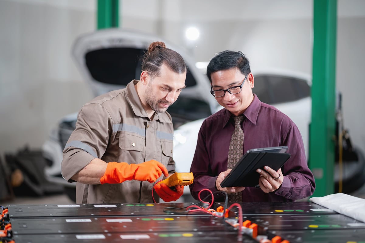 EV technician discussing inspection results with a customer on a tablet in an automotive repair workshop