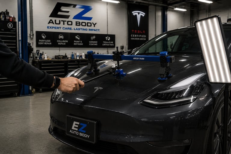 Technician working on black Tesla vehicle hood at EZ Auto Body shop with blue equipment visible